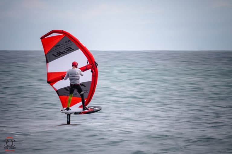 Un homme faisant de la planche à voile dans l'océan avec une voile rouge et blanche