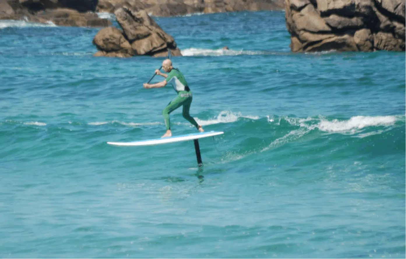 Un homme en combinaison de plongée surfe sur une vague avec une planche de surf.